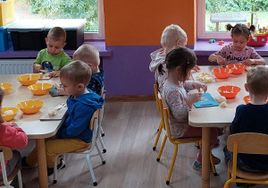 Dzieci siedzą przy stolikach i przygotowują sałatkę warzywną